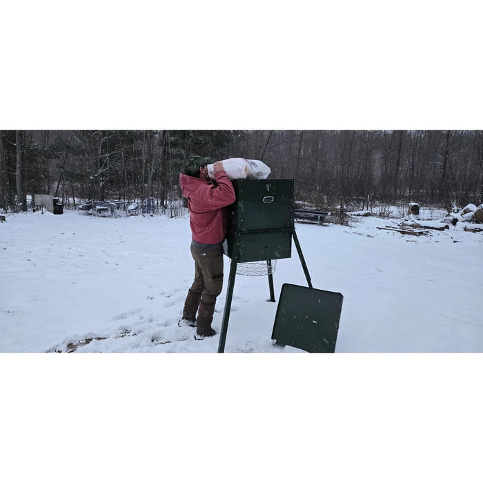 Hunter pouring deer corn into the open hopper of the American Feeder AF300 300 lb Scatter Feeder set up in a snowy field
