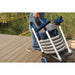 The OASE PondoVac 4 portable pond vacuum loaded on its cart with coiled hose and pipes being carried past a reed pond