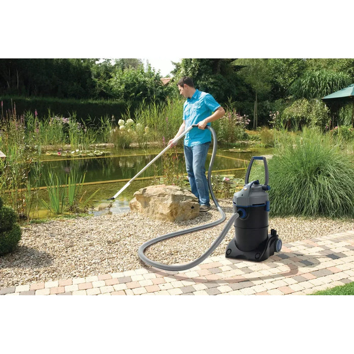 Man vacuuming a garden pond edge with the OASE PondoVac 4 pond and pool vacuum standing on the paved path nearby