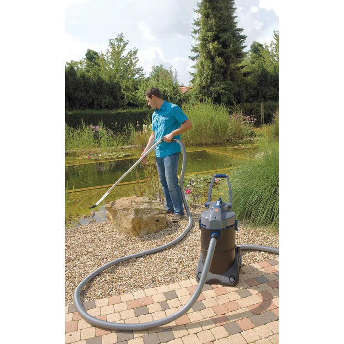 Man using the OASE PondoVac 4 wet vacuum cleaner to clean the edge of a natural garden pond with the extension pipe