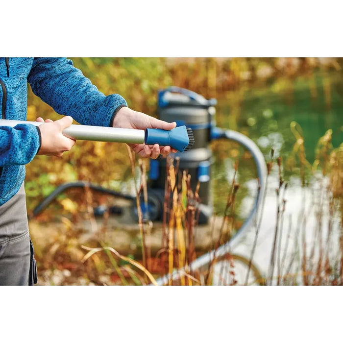 Person attaching the bristle brush nozzle to the aluminium pole of the Oase PondoVac 5 beside a pond outdoors