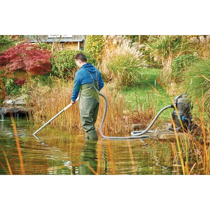 Man in waders vacuuming a garden pond with the Oase PondoVac 5 Pond Vacuum unit positioned on the bank