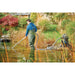 Man in waders vacuuming a garden pond with the Oase PondoVac 5 Pond Vacuum unit positioned on the bank