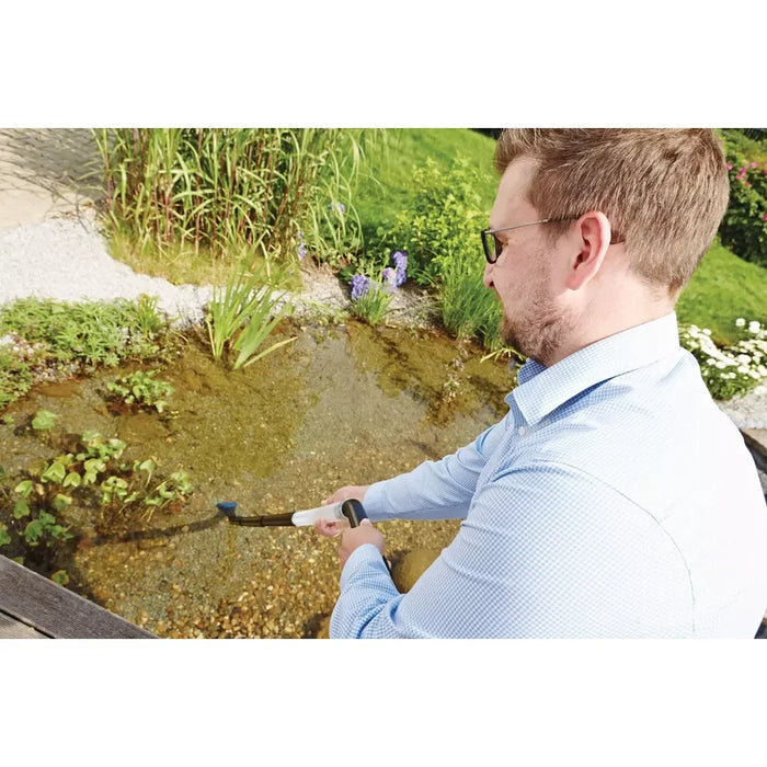 Man using the Oase PondoVac Classic to vacuum sludge from a shallow garden pond with the transparent wand and nozzle