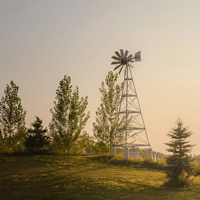 Full 3-leg tower of the Outdoor Water Solutions 3 Leg Steel Windmill Pond Aerator on a grassy hilltop at sunset
