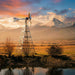 Outdoor Water Solutions Steel Tower Windmill Pond Aerator by a pond at sunset with snow-capped mountains behind