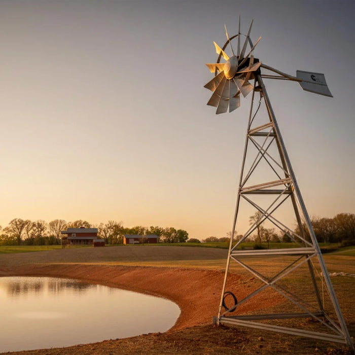 Outdoor Water Solutions 4 Leg Windmill Pond Aerator standing next to a farm pond at sunset with a red barn behind