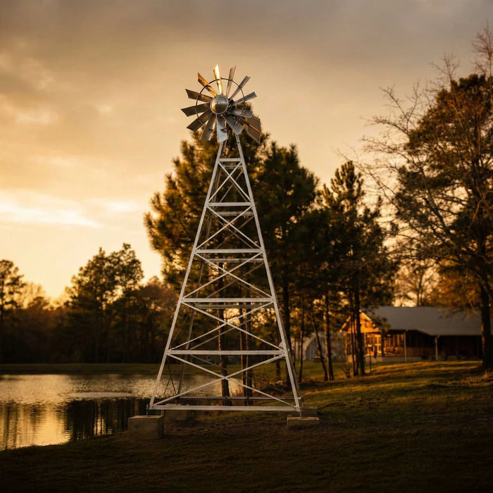 Outdoor Water Solutions 4 Leg Windmill Pond Aerator tall galvanized tower on concrete footers beside a pond at sunset