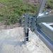 Close-up of the Outdoor Water Solutions 4-Leg Steel Windmill Aerator tower hinge and bolted base bracket on concrete