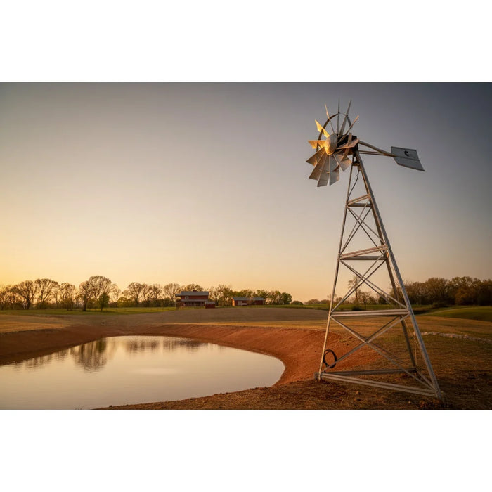 Side view of the Outdoor Water Solutions 3 Leg Windmill Water Aerator by a farm pond at sunset