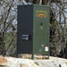 Texas Hunter Pond Fish Feeder with Solar Panel mounted on the side, positioned on a rocky ledge with bare trees in the background